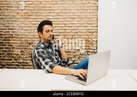 Young man using smartphone at table with laptop Stock Photo