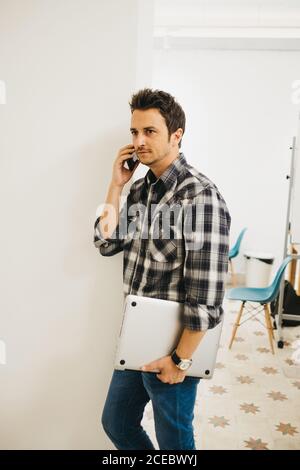 Young man with laptop talking on smartphone Stock Photo
