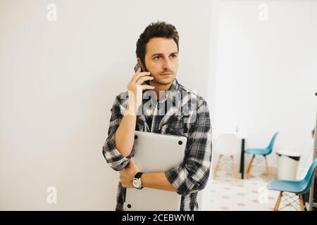 Young man with laptop talking on smartphone Stock Photo