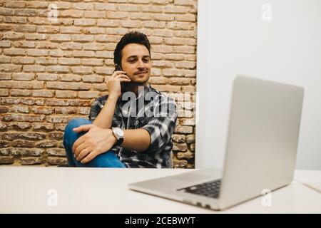 Young man using smartphone at table with laptop Stock Photo