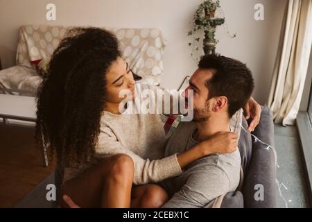 Young multiracial couple hugging on sofa Stock Photo