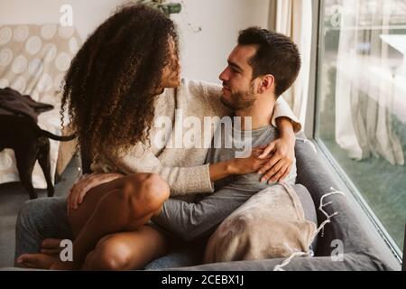 Young multiracial couple hugging on sofa Stock Photo
