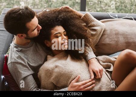 Young multiracial couple hugging on sofa Stock Photo