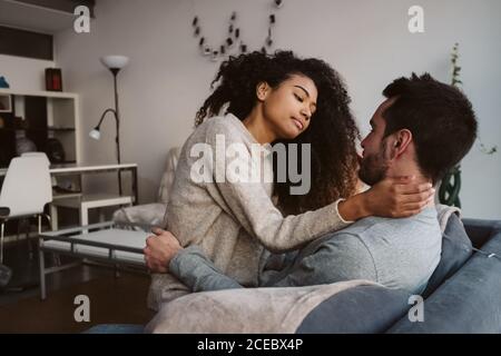 Young multiracial couple hugging on sofa Stock Photo