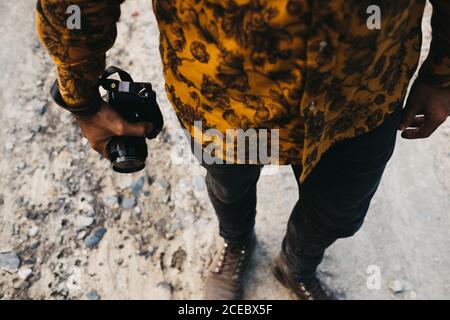 Crop shot from above of man in colorful shirt standing on rocky ground with photo camera in hands Stock Photo
