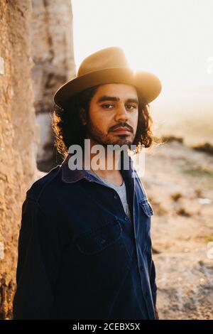 Portrait of adult confident man with beard wearing shirt and hat looking at camera in sunlight outdoors Stock Photo