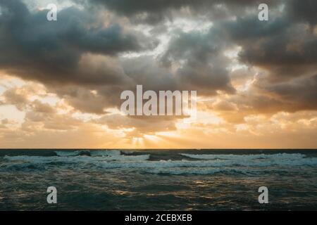 Bright sun setting over waving sea behind thick clouds in Miami Stock Photo