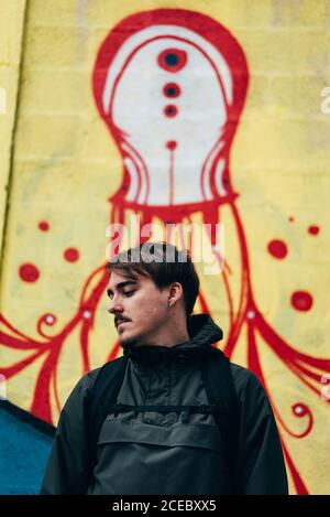 Thoughtful young man standing at graffiti wall with hands in pockets. Stock Photo