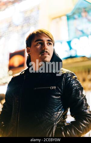 Thoughtful young man standing on illuminated street and looking away. Stock Photo