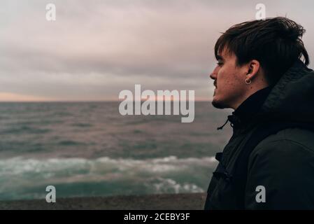 Side view of thoughtful adult man standing at the sea and looking away. Stock Photo