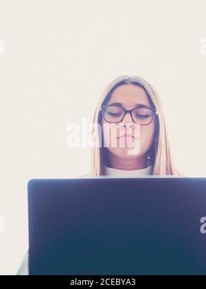 Beautiful pleased teen in eyeglasses using laptop on white background Stock Photo