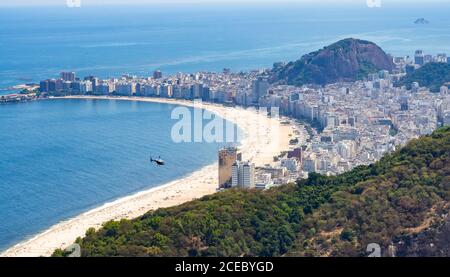 Majestic drone view of distant helicopter flying over sandy beach and modern coastal city in Brazil Stock Photo