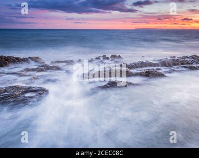 Picturesque view of clean sea water rolling and splashing near rough stones during wonderful sundown Stock Photo