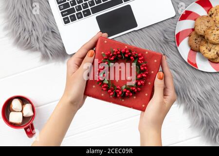 Womans hands holding gift with cocoa and cookies on furry background Stock Photo