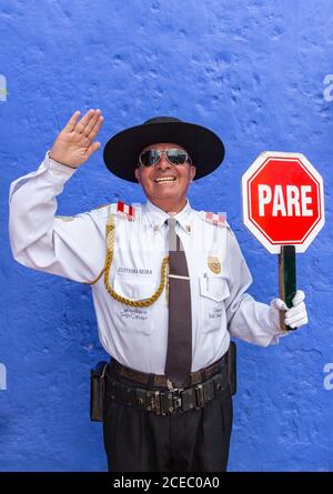 Peru - January, 02 2012: Adult ethnic male in police uniform smiling and looking at camera while standing near blue wall and holding stop sign Stock Photo