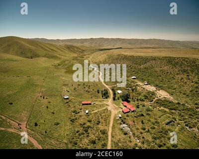 Picturesque aerial view of green terrain with remote houses in bright sunlight among highlands, Argentina