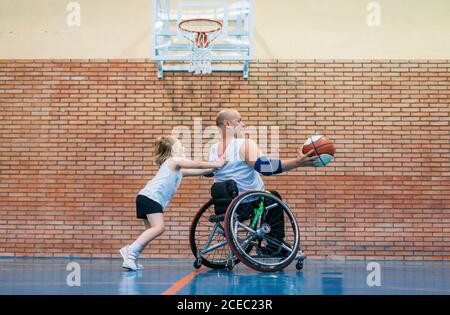 Disabled sport men and little girl in action while playing indoor basketball Stock Photo