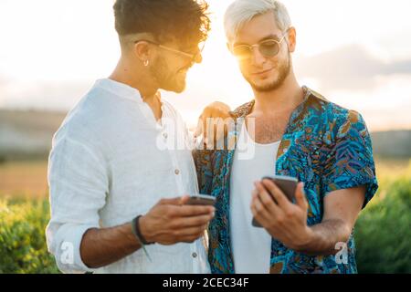 Two smiling men hugging and browsing smartphones while standing in beautiful countryside together Stock Photo
