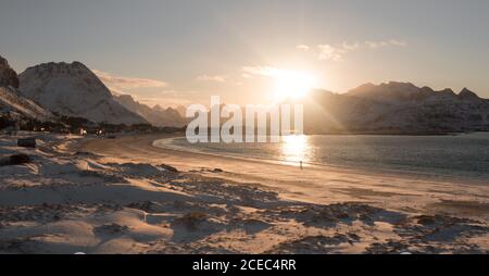 View of snowy shoreline with sandy beach and waves of sea in sunlight on background of mountains, Lofoten island Stock Photo