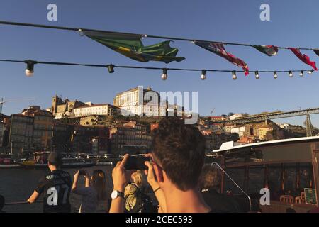 PORTO, PORTUGAL - JANUARY 23, 2019: Group of tourists on taking photos of old city exterior while having sailing tour on boat Stock Photo