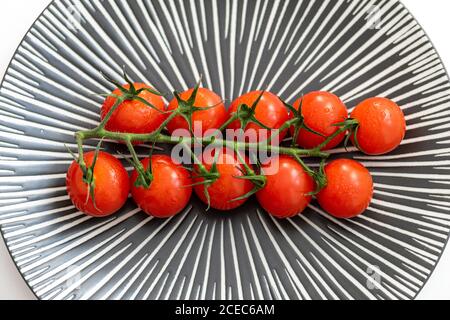 a close up image of a vine of tasty cherry tomatoes on a patterned grey plate Stock Photo