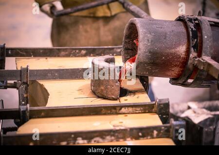 Crop male in uniform pouring molten metal from crucible in form on little foundry Stock Photo