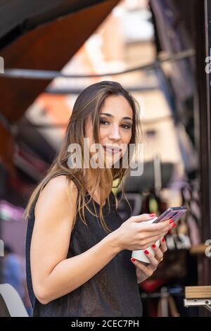 Woman with drink and smartphone near outdoor cafe Stock Photo
