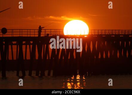 A man fishing in the early morning light as the sun rises over Blyth pier in Northumberland on the first day of Meteorological autumn. Stock Photo