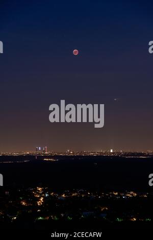 Breathtaking view of red moon over brightly illuminated Madrid during eclipse Stock Photo