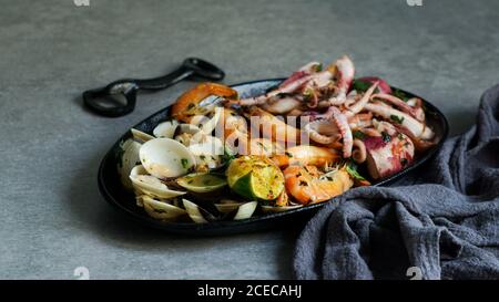 From above tasty grilled octopus, oysters and shrimps with lime and herbs on cast iron plate near napkin Stock Photo