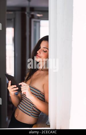 Young Woman standing near window and using mobile phone Stock Photo