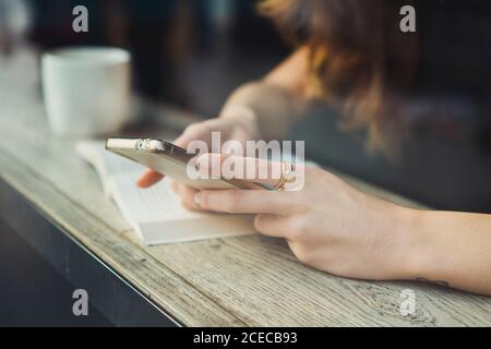 Crop unrecognizable Woman sitting at window in cafe and using smartphone Stock Photo