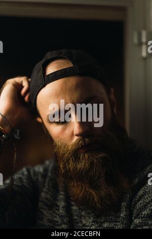Portrait of young man with beard wearing cap and looking thoughtfully down. Stock Photo