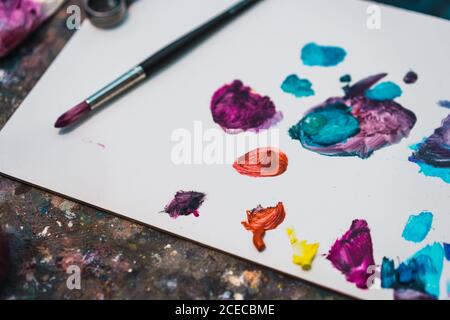 Paintbrush lying on white paper with stains of colorful paints. Stock Photo