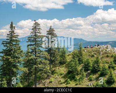Hiker resting on a rock in the distance and admiring the beautiful mountain lanscape. Piatra Mare (Big Rock) mountains in Romania. Stock Photo