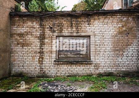 Big window boarded with shabby lumber planks and located on brick wall of grungy building in small settlement Stock Photo