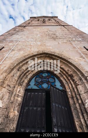 From below shot of beautiful door and shabby walls of majestic old church on background of cloudy sky Stock Photo