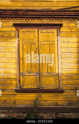 Window with closed shutters located on lumber wall of yellow countryside house Stock Photo
