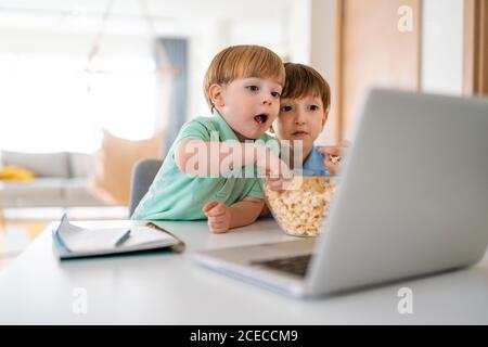 Cute children playing, watching movie on laptop at home. Digital addiction concept.