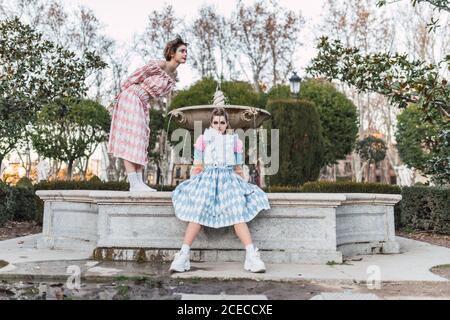 Two young women in theatrical costumes acting near old fountain in beautiful park Stock Photo