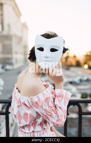 anonymous young Woman wearing theatrical costume and white mask while acting on street of city Stock Photo