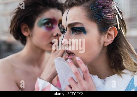 Two young women with theatrical makeup and unusual clothes sharing secret while performing on city street Stock Photo