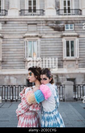 side view of Two young women with theatrical makeup and unusual clothes performing and hugging on city street Stock Photo