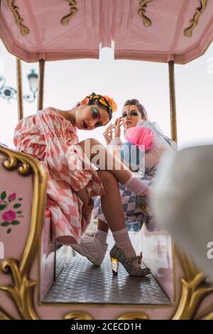 Two pretty young women with theatrical makeup?and costumes looking at camera while sitting on amazing roundabout in amusement park Stock Photo