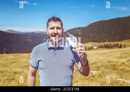 Portrait of mature man taking off protective face mask and breathing fresh air on top of the mountains Stock Photo