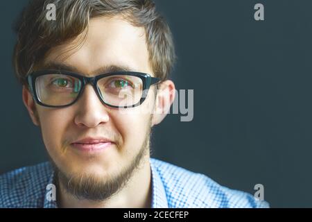 Man software developer engineering student in glasses. Close up smiling young businessman wearing eyeglasses, looking at the camera against gray wall background with copy space. Stock Photo