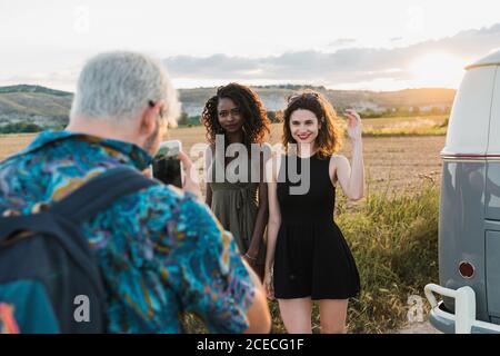 unrecognizable guy using smartphone to take photo of two lovely women while spending time in nature together Stock Photo