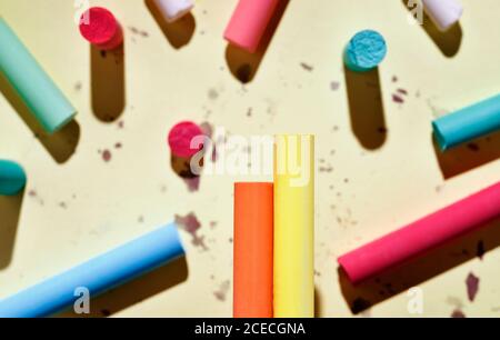 Multicolored thick sticks of chalk on colored background , in the foreground two pieces orange and yellow in focus Stock Photo