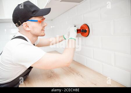 Ceramic tile with chamfer hands in process of laying white rectangular tiles on kitchen wall Stock Photo