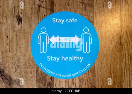 Coronavirus pandemic precautions: blue social distancing reminder sticker on a wooden shop floor in Petworth, a town in West Sussex, southeast England Stock Photo